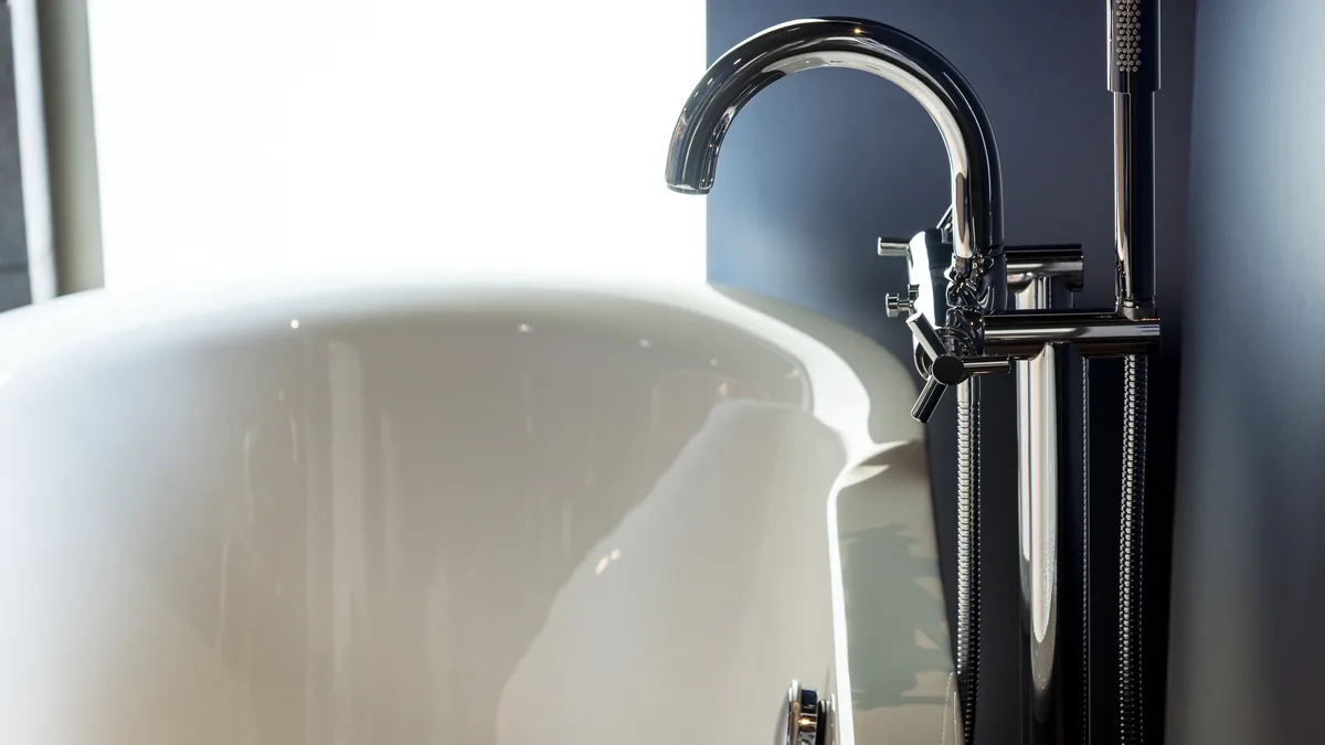 Chrome bath mixer tap beside a white freestanding bathtub