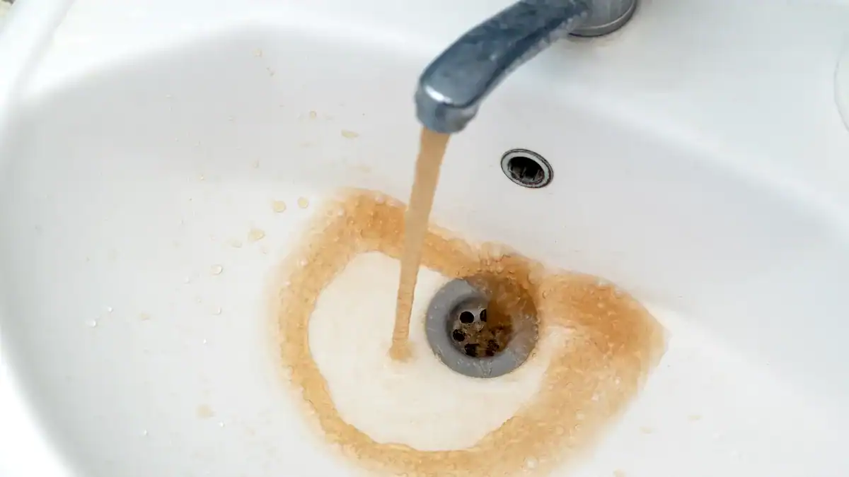 Brown water running from a tap into a white bathroom basin