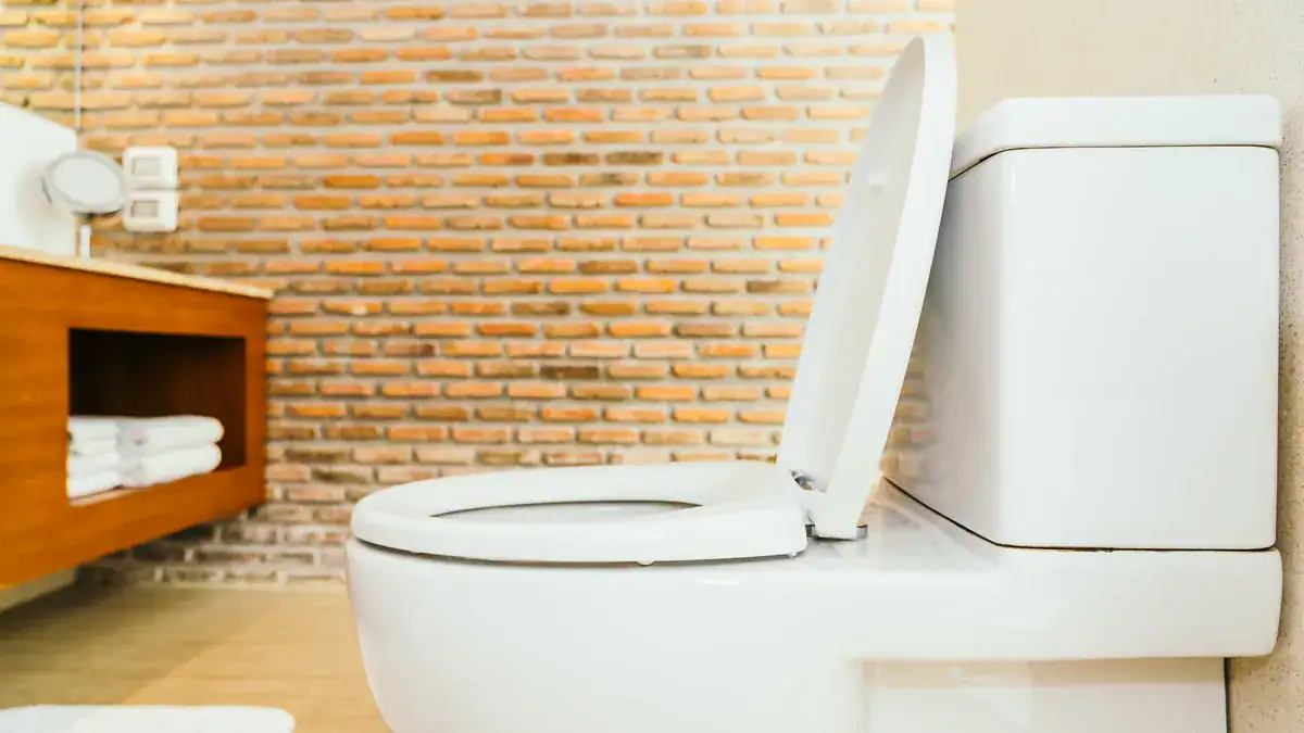White close-coupled toilet with the seat raised in a brick-walled bathroom