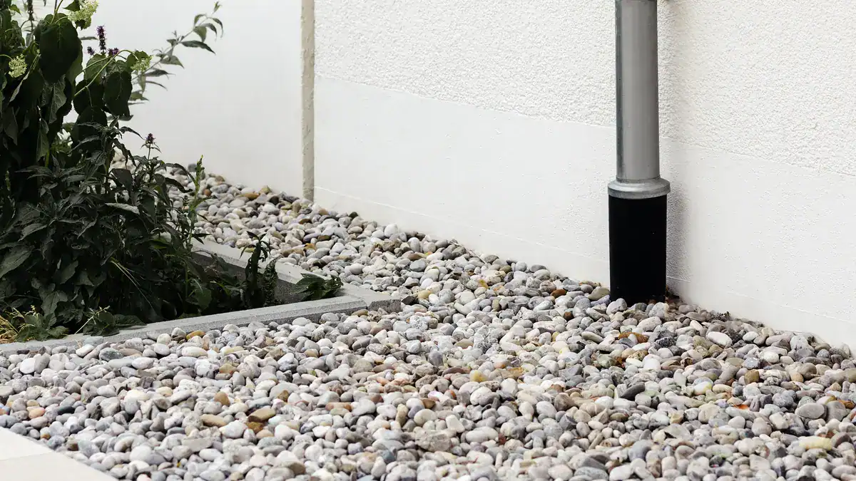 Downpipe running into a gravel drainage bed beside a house wall