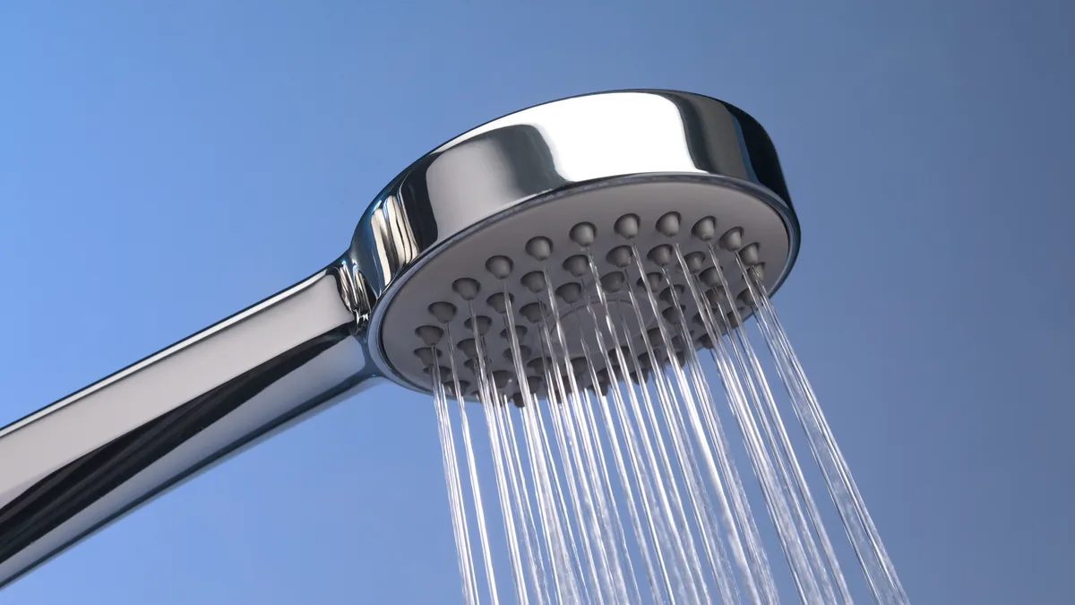 Chrome shower head spraying water against a blue background