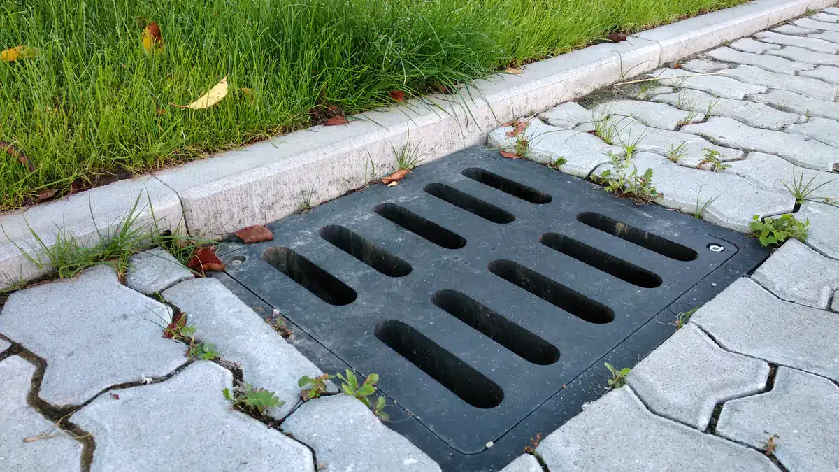 Black stormwater pit grate set into paving beside a lawn